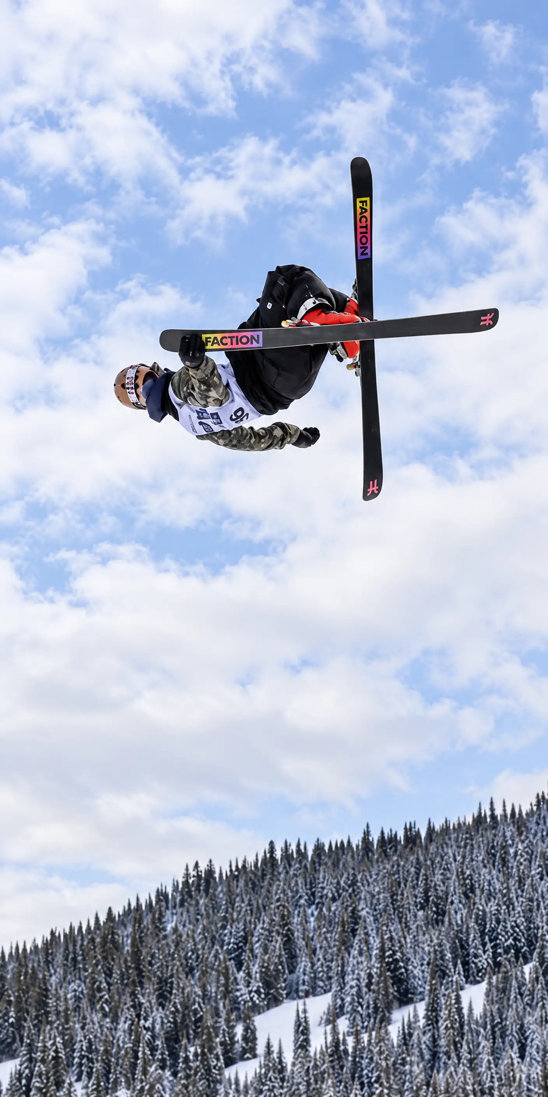 Byron Lambert upside down in the air against blue sky, skis crossed