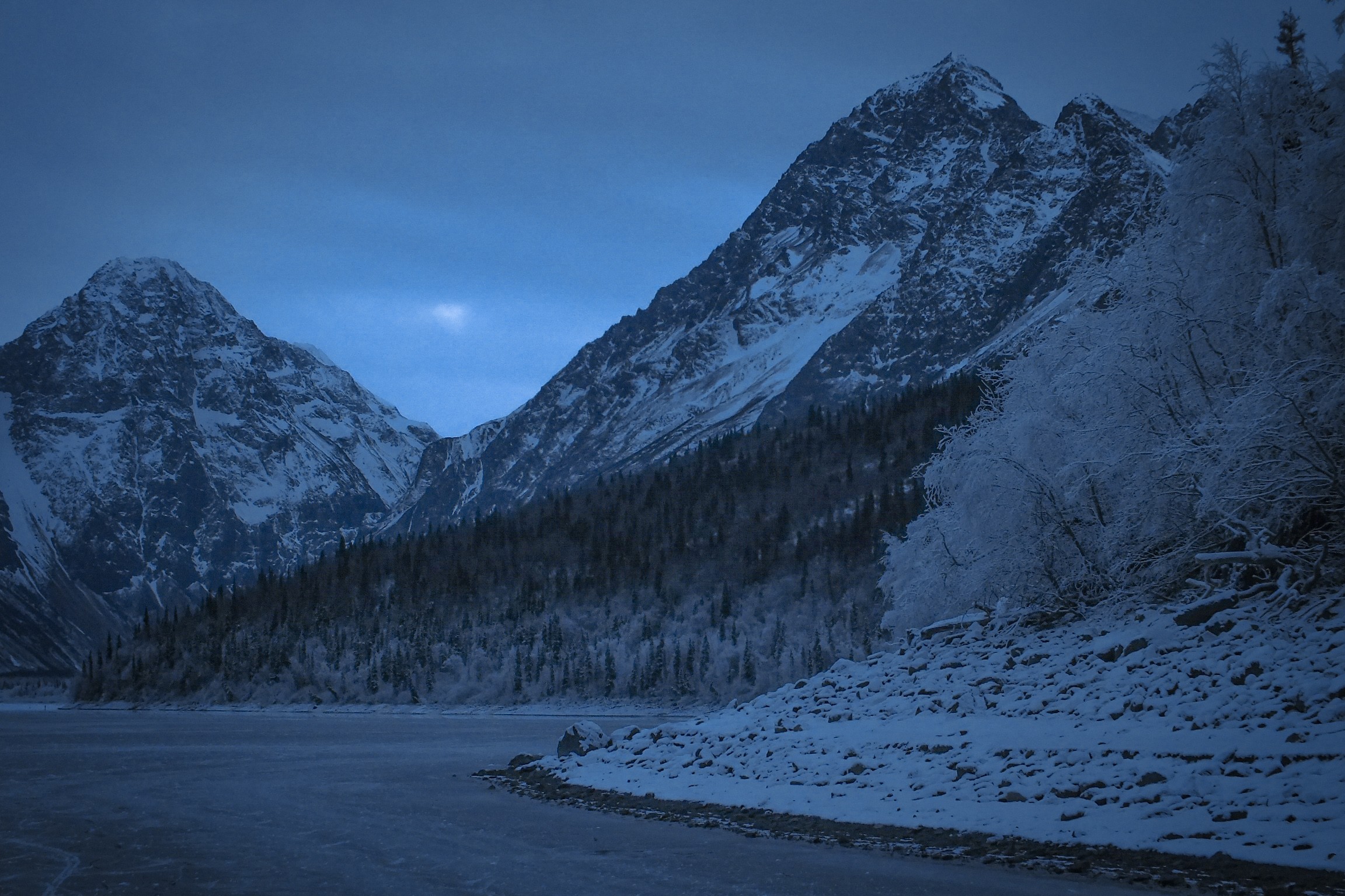 Snowy peaks above a lake in early morning blue light, photo by Byron Lambert