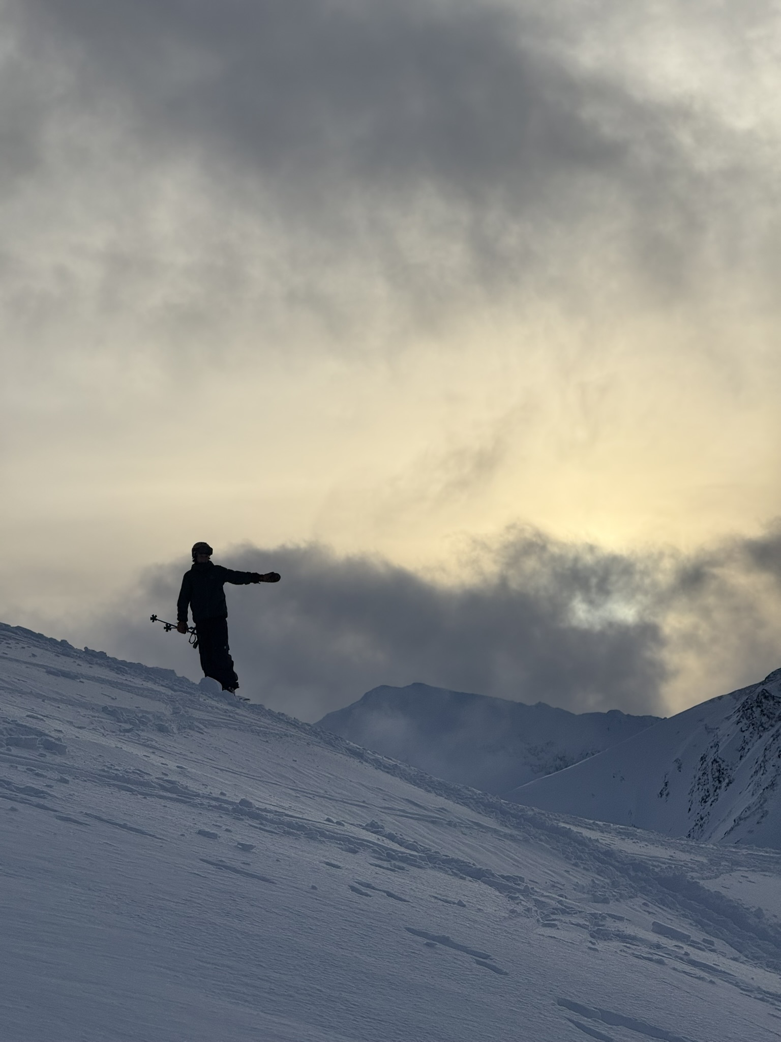 A skier silhouetted on a ridge under dramatic clouds